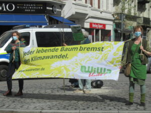 2 Aktivist*innen tragen ein Banner durch die Straße. Darauf zu lesen: „Jeder lebende Baum bremst den Klimawandel" und das Logo "WiWa bleibt".