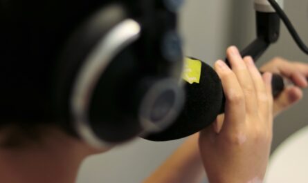 Vordergrund: schemenhafter Kopf mit Kopfhörern, ein Mikrofon in der Hand im Bildhintergrund
