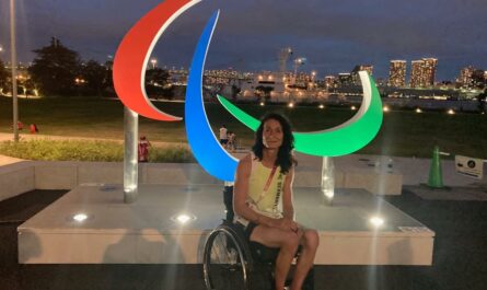 Sylvia-Pille-Steppat in Tokio vor dem Symbol der Paralympics und der abendlichen Silhouette der Stadt.
