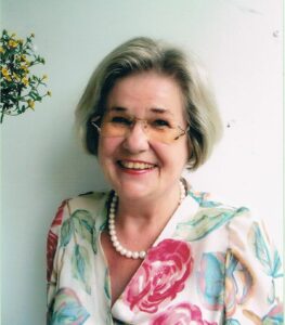 Edda Sievers lächelnd an ihrem 70. Geburtstag in einem geblümten, hellen Kleid mit Perlenkette und randloser Brille