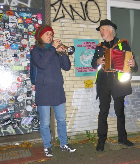 Sabine Braun (Kornett) und Ulrich Kodjo Wendt (Zieharmonika) stehen vor einer Hauswand und musizieren.