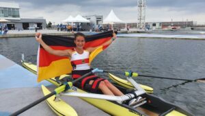 Pararuderin Sylvie Pille-Steppat in ihrem Ruderboot auf dem Wasser mit einer Deutschlandflagge in den Armen