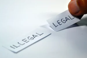 aif weißem Hintergrund liegt ein Zettel mit der Aufschrift "Illegal", eine Hand legt einen mit der Aufschrift "Legal" daneben