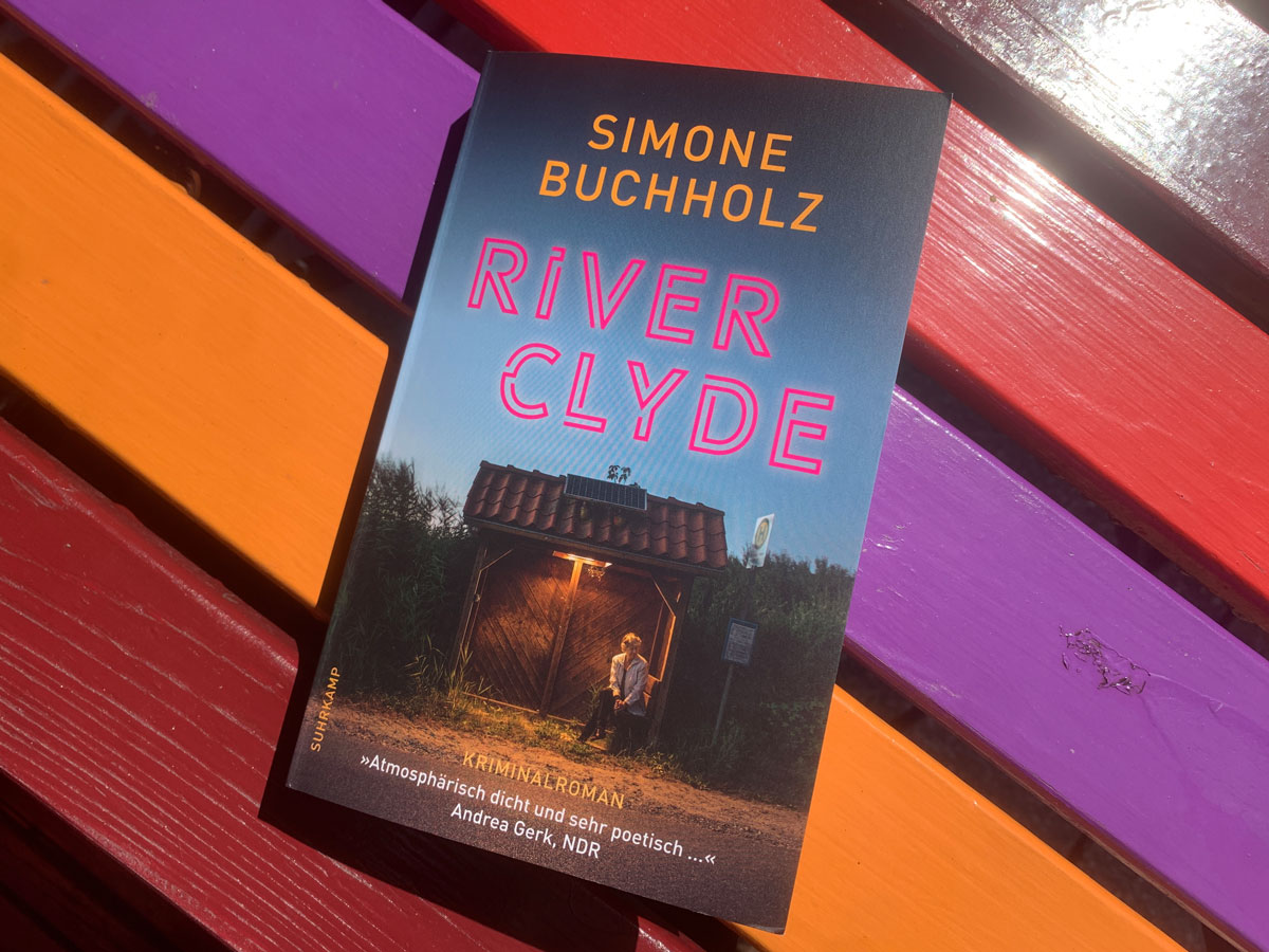 Das Taschenbuch River Clyde von Simone Buchholz auf einer bunten Platte.