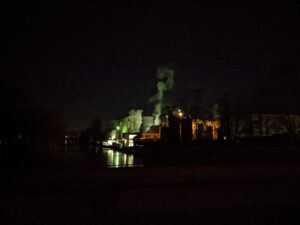 Es ist dunkel, die Fabrik ist grün erleuchtet, aus ihren Schornsteinen steigt Dampf in den Himmel.