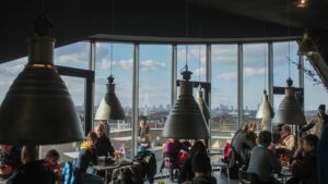 Ein moderner Caféraum, Aussicht durch sekrechte Panoramafenster auf den blauen Himmel und die Stadt