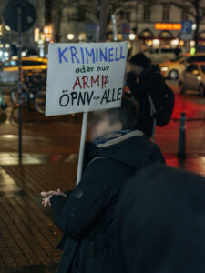 Eine Person hät ein Schild in der Hand auf dem steht: Kriminell oder nur arm? ÖPNV für Alle.