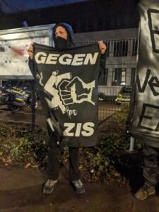Ein Demonstrierender hät ein Transparant mit der Aufschrift "Gegen Nazis" und einer Faust, die ein Hakenkreuz zerstört hoch.