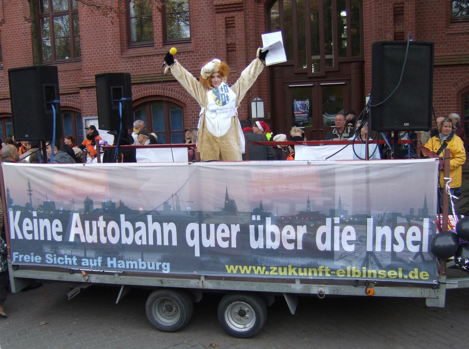 Eine Demo vor dem Wilhelmsburger Rathaus. Im Vordergrund unten das Transparent: Keine Autobahn quer über die Insel. Darüber eine Aktivistin, die beide Arme in die Luft wirft.