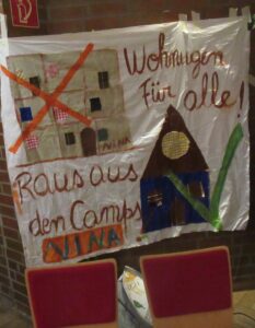 Ein Transparent der Nina-Gruppe mit dem Bild eines rot durchgekreuzten Hauses und mt der Aufschrift: Wohnungen für alle! Raus aus den Camps