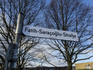 Auf einem Straßenschild steht "Fatih-Saraçoğlu-Straße, im intergrund ein blauer Himmel und kahle Bäume.