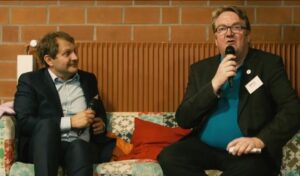 Links Umweltsenator Jens Kerstan auf einem bunten Sofa mit Lars Maier rechts. Im Hintergrund ein hellbrauner Heizkörper.