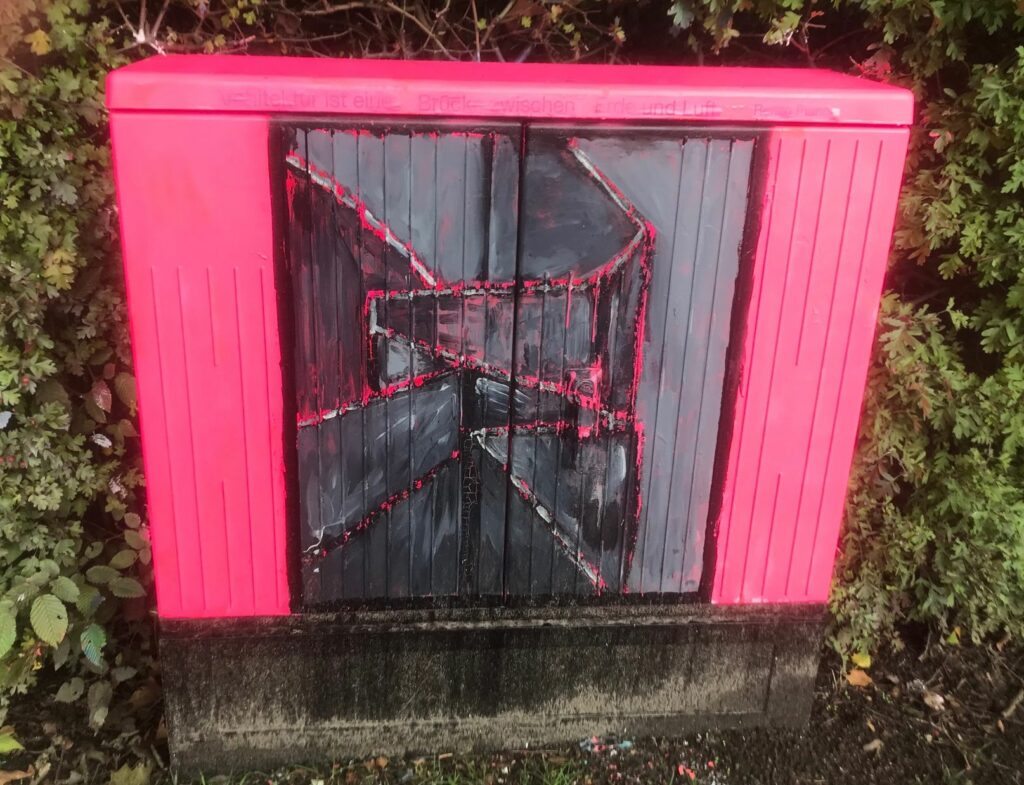 Ein Stromkasten, pink angemalt, mittig ein schwarzes Quadrat, durchzogen von pinken Linien.