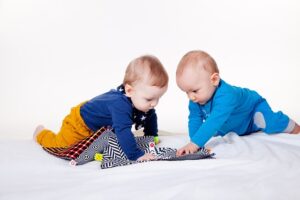 Zwei Krabbelkinder spielen zusammen auf einer Decke.