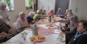 Senior*innen sitzen gutgelaunt um eine Kaffeetafel.