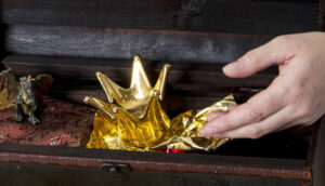 Eine Hand holt eine kleine goldene Krone aus einer Holzkiste.