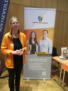 Eine Frau in orangener Jacke vor dem Roll-Up der Stadtreinigung