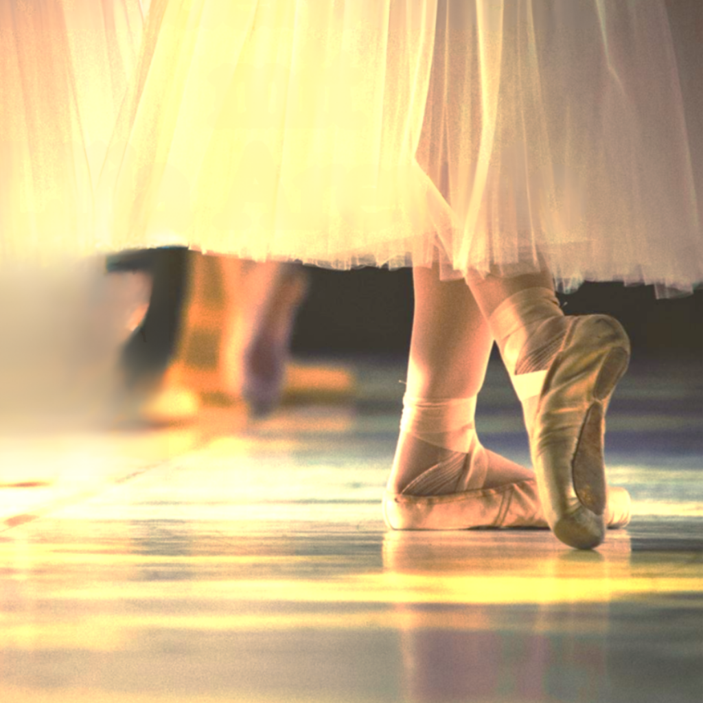 Zwei Füße in Balletscuhen in Balletposition, ein weißes Kleid.