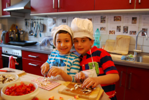 Zwei Kinder mit Kochmützen kochen in einer Küche.