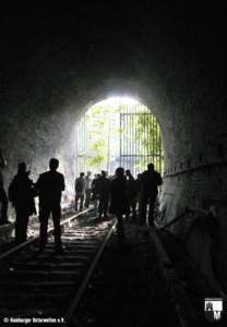 Menschen laufen durch einen runden Eisenbahntunnel auf den Ausgang im Tageslicht zu.