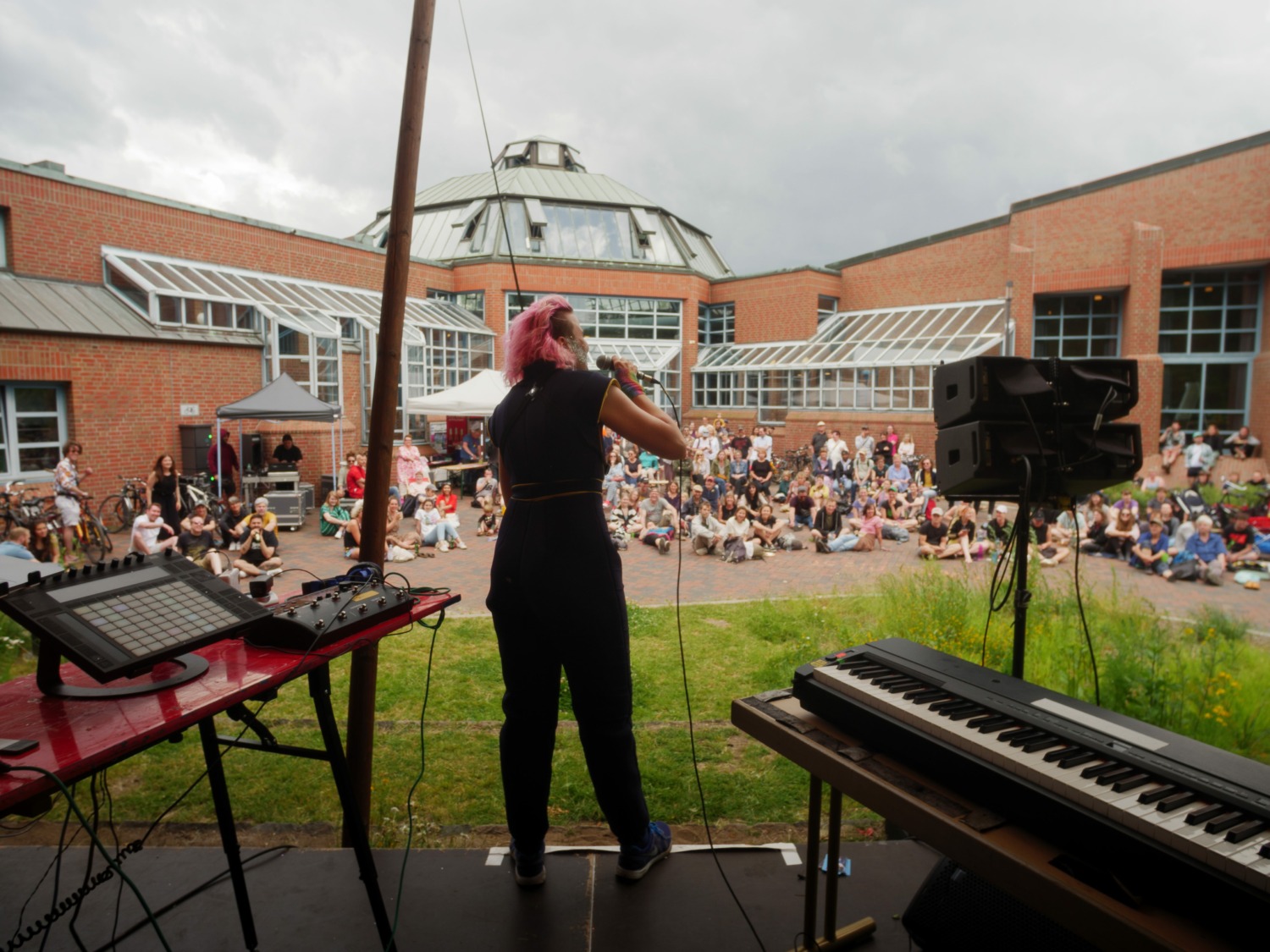Blick von hinter einer Bühne auf eine spielende Künstlerin und ihr Publikum vor dem Hintereingang des Bürgerhaus Wilhelmsburg