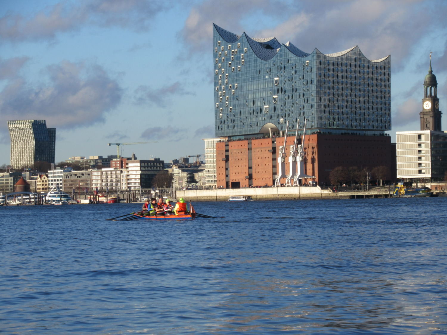 Foto von Menschen in einem Ruderbot im Hamburger Hafen, rechts davon die Elbphilharmonie
