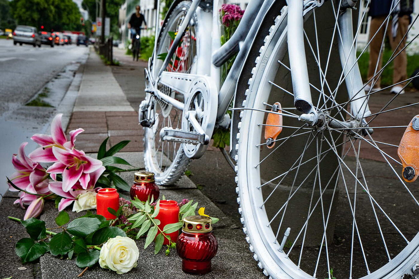 Ein weiß angestrichenes Fahrrad mit Blumen, die davor auf der Straße liegen