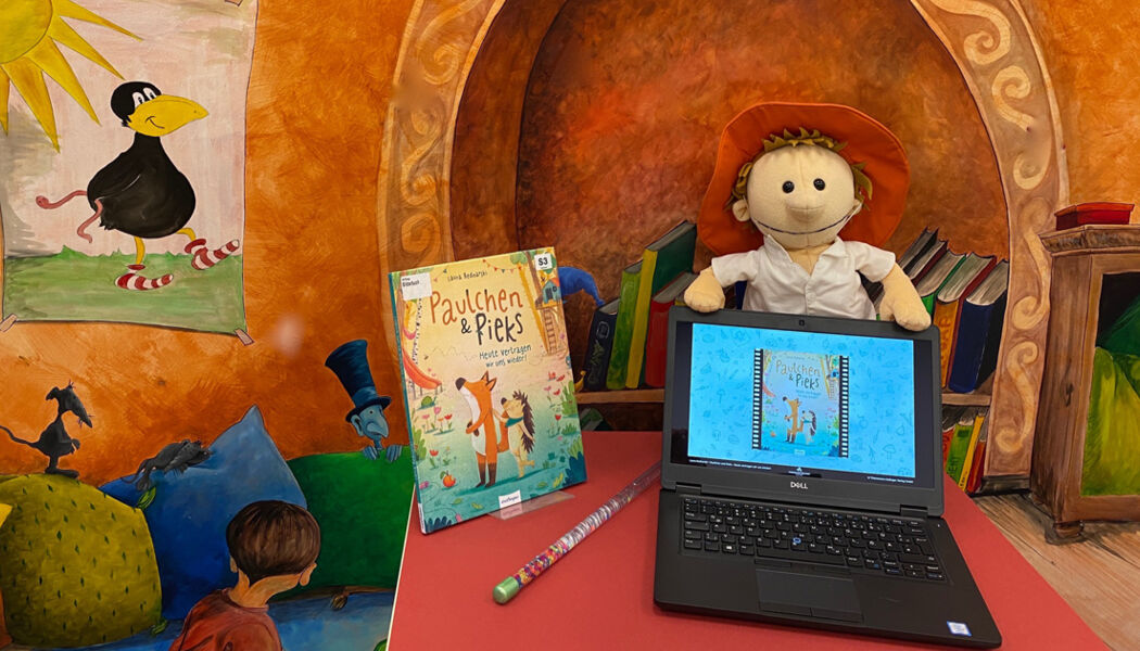 Eine bunte Lese und Spielecke für Kinder mit einem präsentierten Bilderbuch, einem Stofftier und einem kleinen Laptop