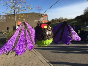 Eine grpße bunte Fledermaus hängt an einem Seil über einem Betonplatz