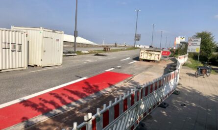 Baustellenabsperrung in rot weiß gestreift, Am Fuße der Argentinienbrücke, rote Bike Lane umzingelt von Containern, rechts am Rand des Bildes steht ein Lastenrad an der Absperrung