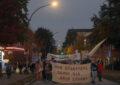 Ein Demontrationszug von vorne, der eine Straße entlangläuft, auf dem Fronttransparent steht: "Den Stadtteil denen, die drin leben". Links im Bild eine Tankstelle