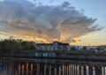 Über einer alten, mit Graffiti besprühten Lagerhalle auf der anderen Seite eines Kanals ziehen sich Wolken am abendlichen Himmel zusammen