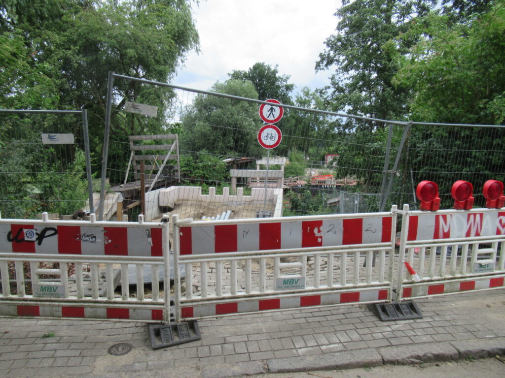 Die Baustelle mit dem Bauzaun im Vordergrund. Im Hintergrund die Pfeiler der Brücke