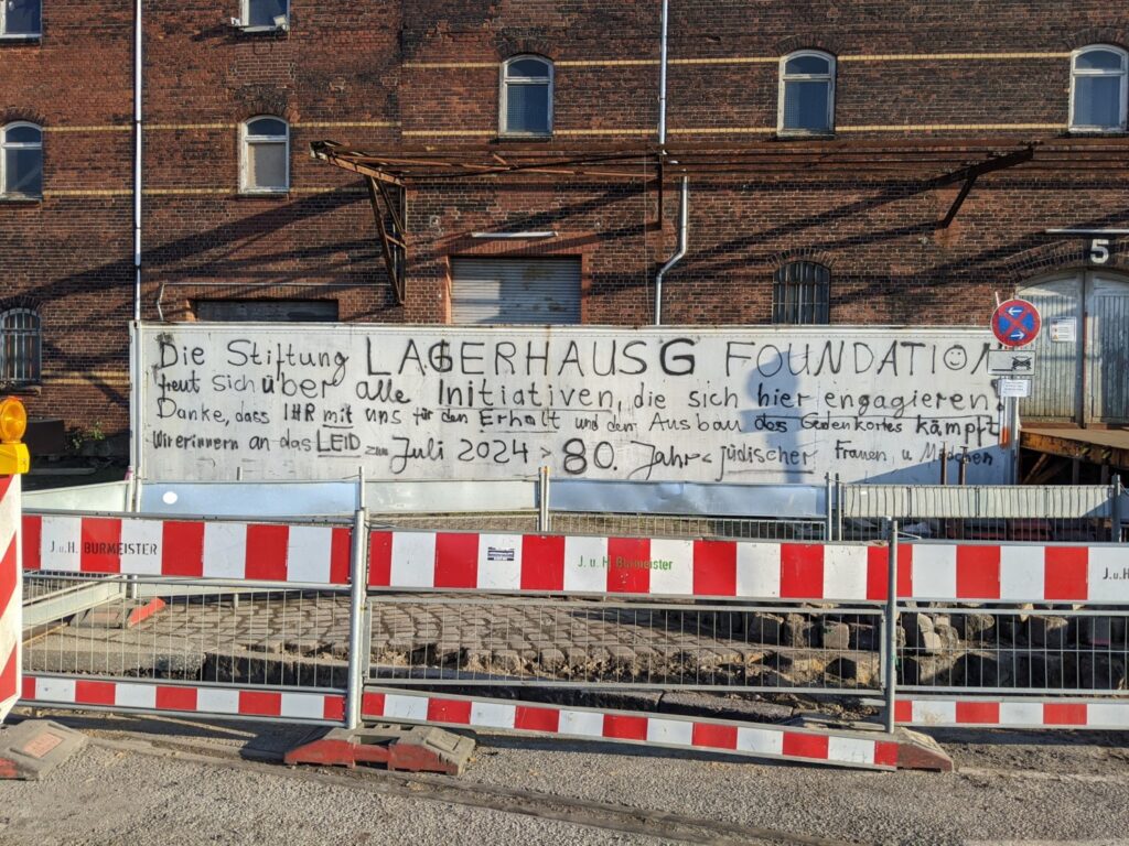 Vor einem Backsteingebäude steht ein weißer Baucontainer. Auf dem ist ein Schriftzug gesprüht (siehe BU), davor eine Baustellenabsperrung