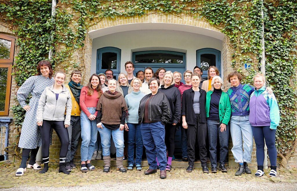 Eine Gruppe lächelnder Menschen steht vor einer Tür eines mit Efeu bewachsenes Gebäudes