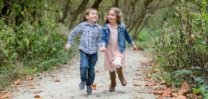 Zwei Kinder laufen lachend und Händchenhaltend durch einen Park