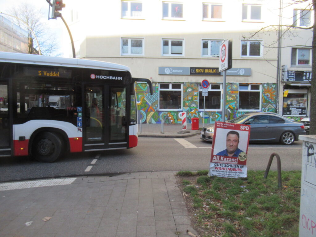 Ein Bus biegt von links kommend rechts in die Veringstraße und holt in den Gegenverkehr aus. Rechts im Bild ca. 3 Meter vor dem Bus steht ein Auto an der Haltelinie vor der Ampel.