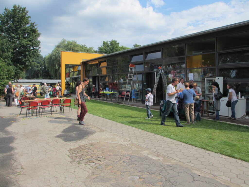 Blick auf die Ateiers vom Hof aus. Im Hintergrund eine Gruppe feiernder Besucher*innen.