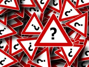 Viele dreieckige Straßen-Warnschilder mit rotem Rand und schwarzem Fragezeichen in der Mitte liegen durcheinander.