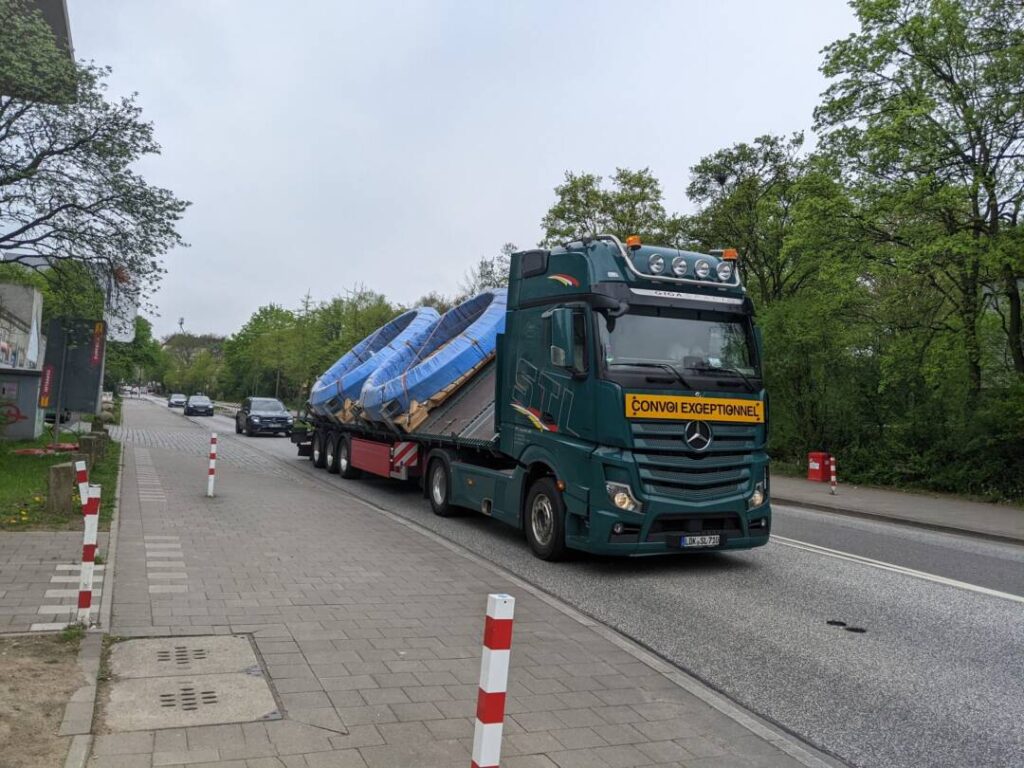 Ein großer LKW, der zwei Pools geladen hat, fährt durch eine schmale Straße