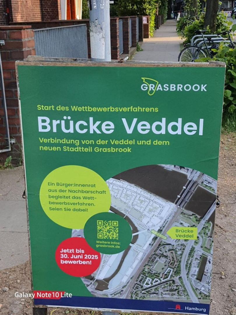 Ein Straßenaufsteller mit einem grünen Plakat, auf dem der Entwurf für eine Brücke zu sehen ist, dazu die Infos