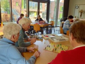 Ältere Menschen sitzen an einem Tisch, manche spielen Mensch-ärgere-dich-nicht