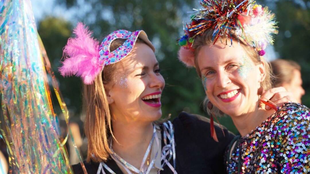 2 Frauen mit buntem Kopfschuck bzw. Mase, uaren sich und lachen sich an