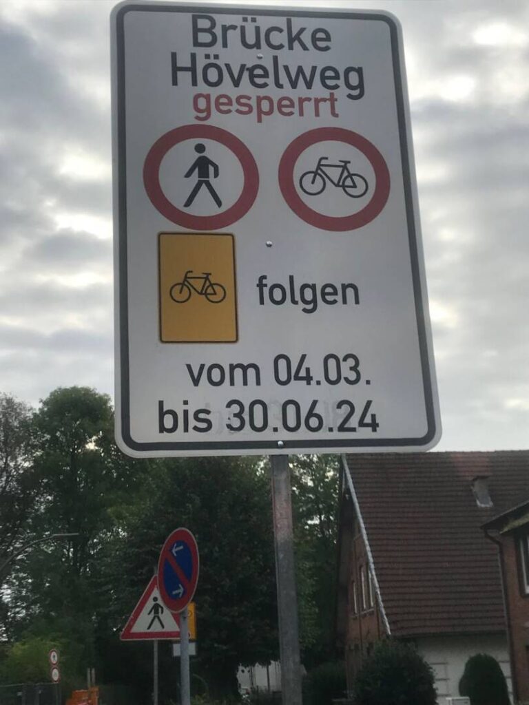 Das Hinweisschild: Brücke Hövelweg gesperrt. Darunter Fußgängerverbot, daneben Radfahrverbot. Darnter das gelbe Schild mit einem schwarzen Fahrrad, daneben der Hinweis folgen. Darunter steht: vom 04.03. bis 30.06.24