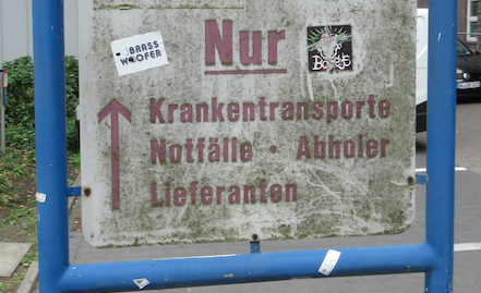 veredrecktes Schild mit der Aufschrift: Krankentransporte, Notfälle, Abholer, Lieferanten und Richtungspfeilen