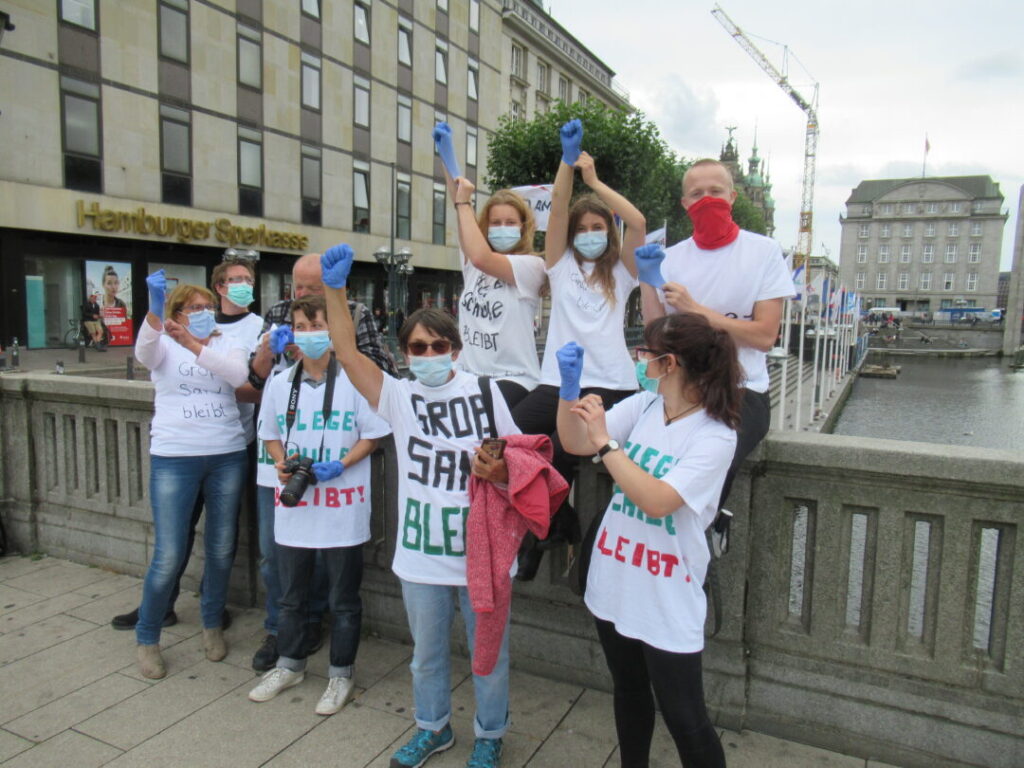 7 jungemenschen mit Parolen-T-Shirts und bauen Corona-Masken auf der Reesendammbrücke recken ihre Faust mit blauem Handschuh in die Luft