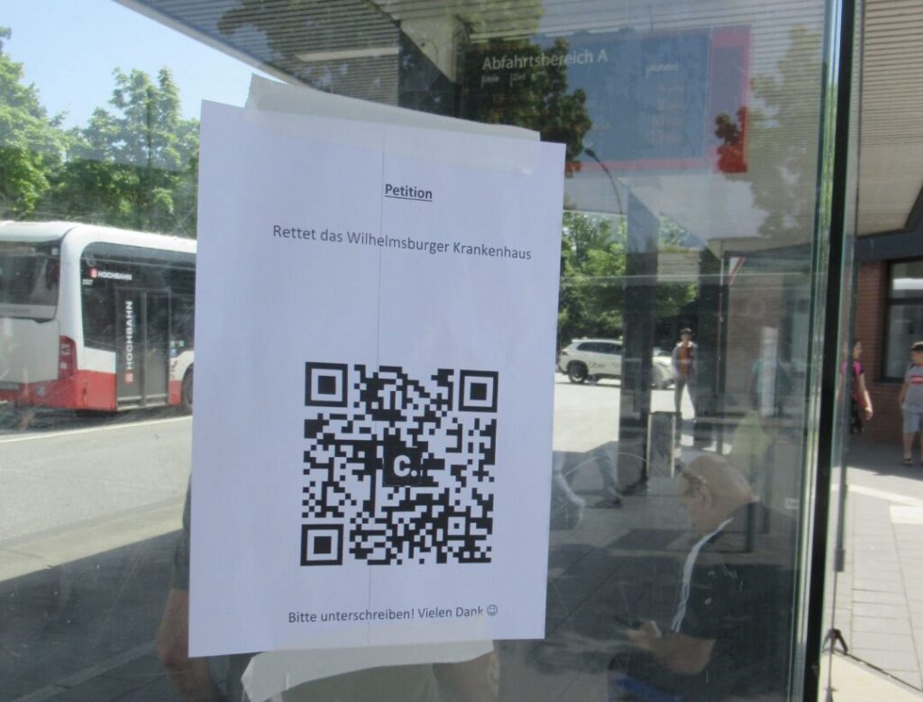 Zettel mit QR-Code an der Glaswand einer Bushaltestelle. Darüber steht: Petition - Rettet das Wilhelmsburger Krankenhaus