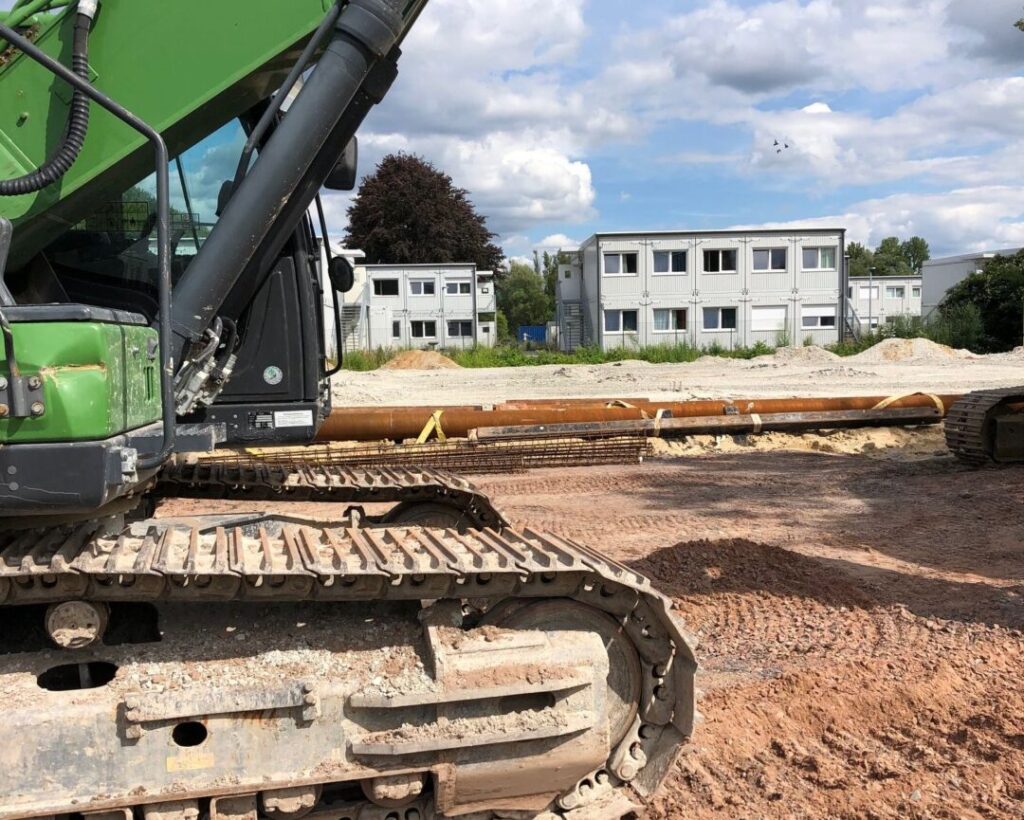 Links eine Planierraupe auf Sandgrund. Im Hintergrund Wohncontainer.