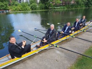 5 Herren im Ruderboot am Ufer