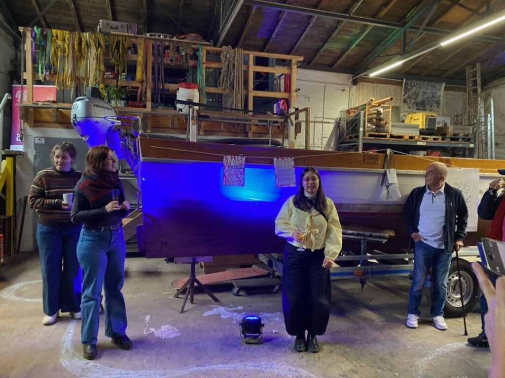 Vier Menschen vor einem blau angestrahltem Boot.